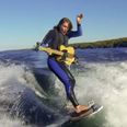 Video: A guy playing electric guitar while wake boarding out the back of a speedboat